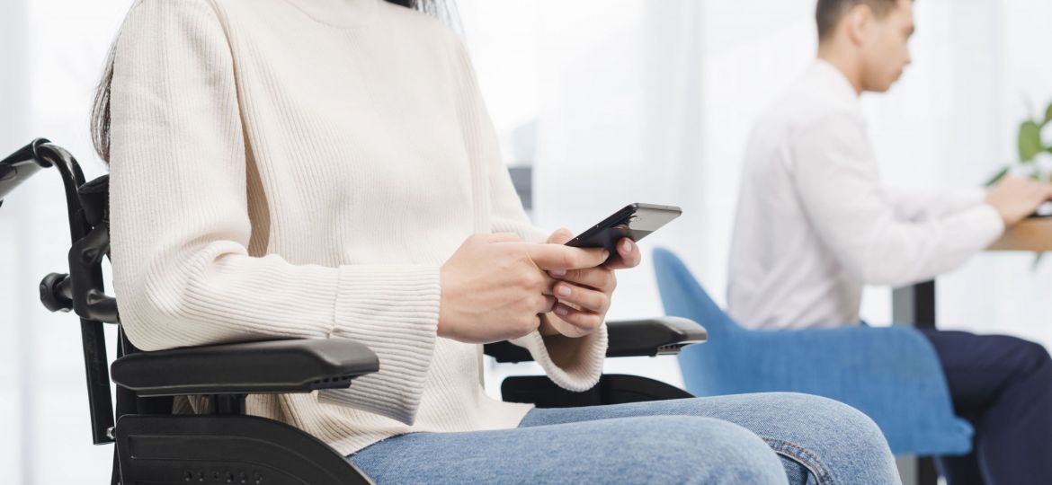close-up-of-a-smiling-disabled-young-woman-sitting-on-wheelchair-using-mobile-phone-in-front-of-his-male-colleague (1)