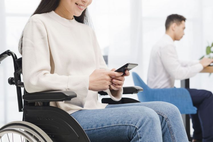 close-up-of-a-smiling-disabled-young-woman-sitting-on-wheelchair-using-mobile-phone-in-front-of-his-male-colleague (1)